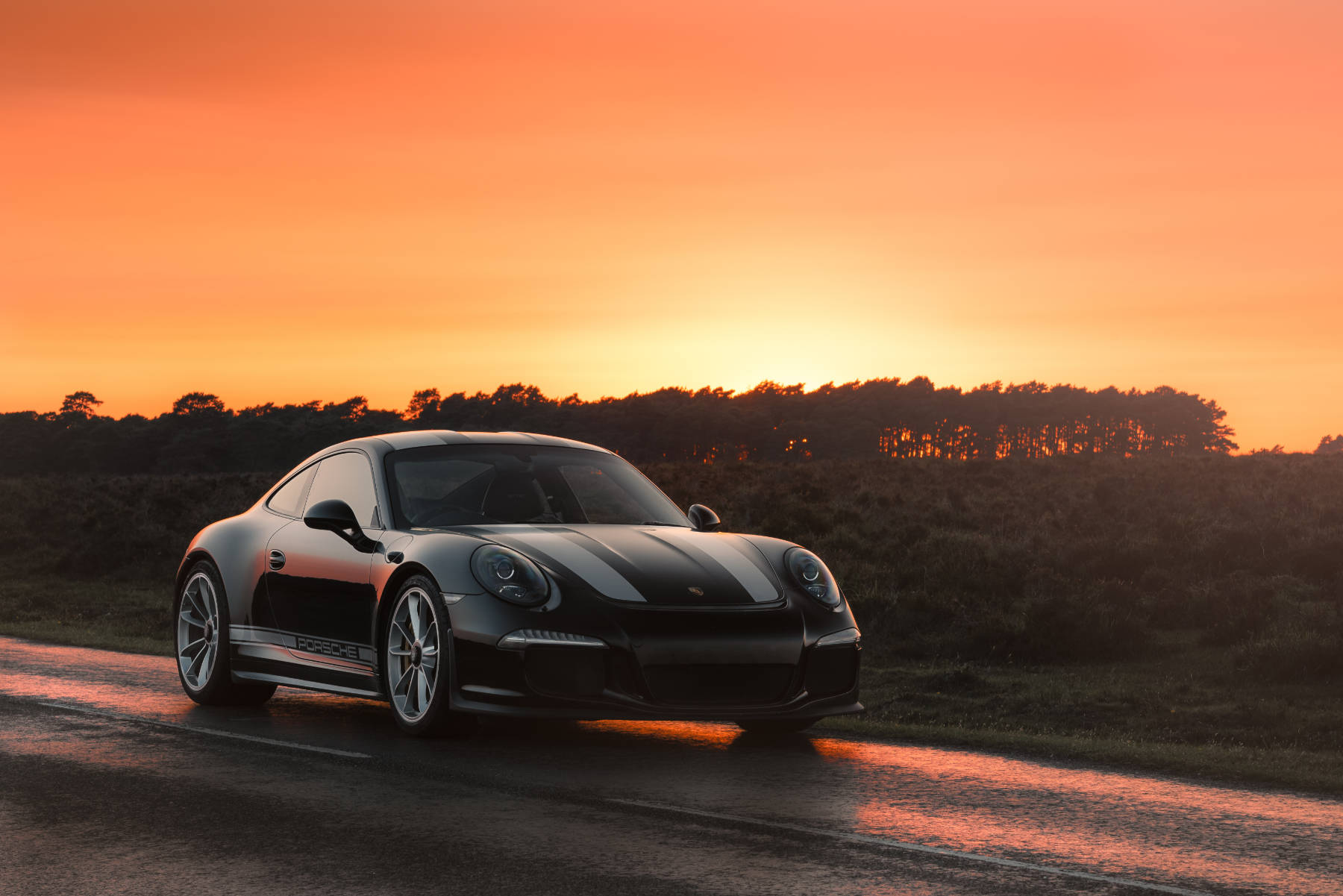 Black Porsche with racing stripes in the sunset